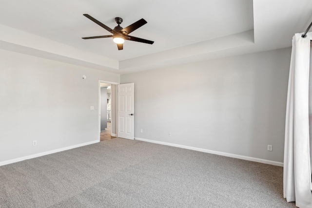 carpeted empty room featuring ceiling fan and a raised ceiling