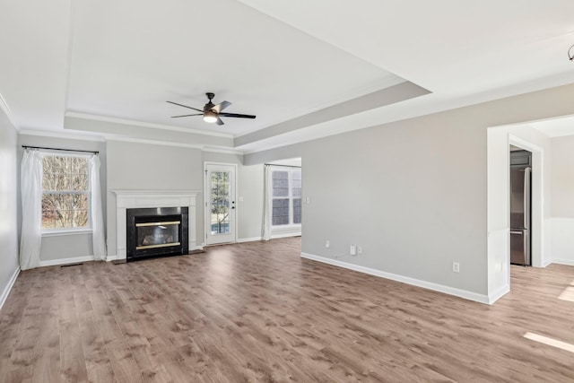 unfurnished living room featuring ceiling fan, plenty of natural light, light hardwood / wood-style flooring, and a raised ceiling