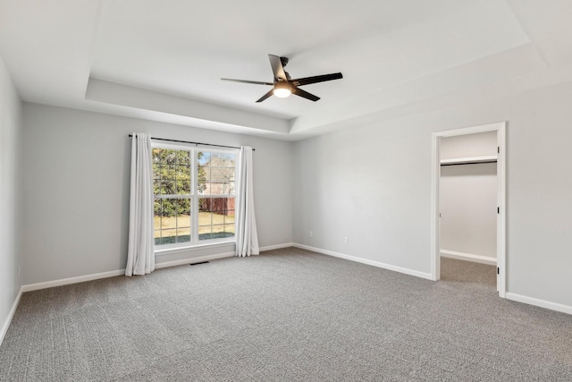 interior space with ceiling fan, a tray ceiling, and carpet flooring