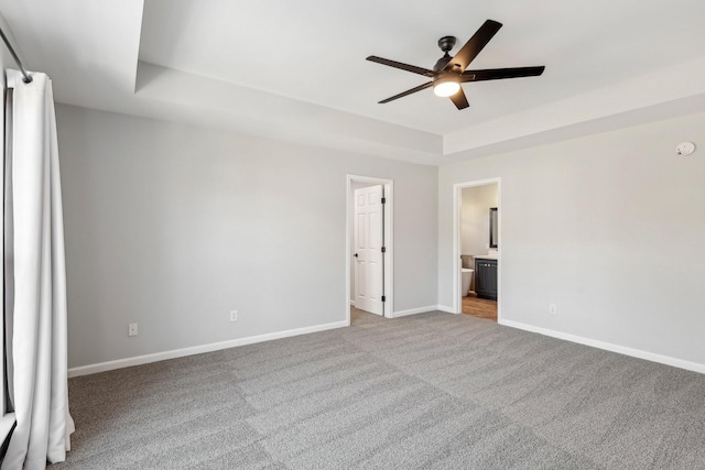 unfurnished bedroom featuring light carpet, ceiling fan, connected bathroom, and a tray ceiling