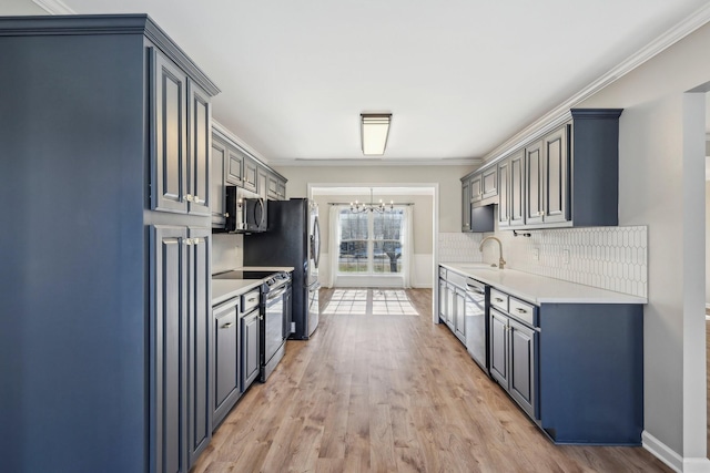 kitchen with an inviting chandelier, light hardwood / wood-style floors, appliances with stainless steel finishes, ornamental molding, and sink