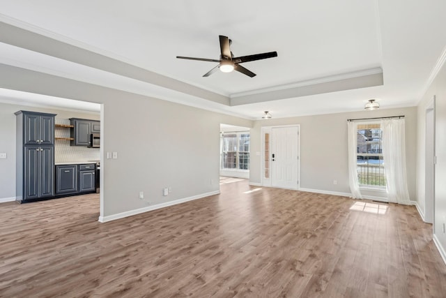 unfurnished living room with a raised ceiling, ceiling fan, ornamental molding, and wood-type flooring