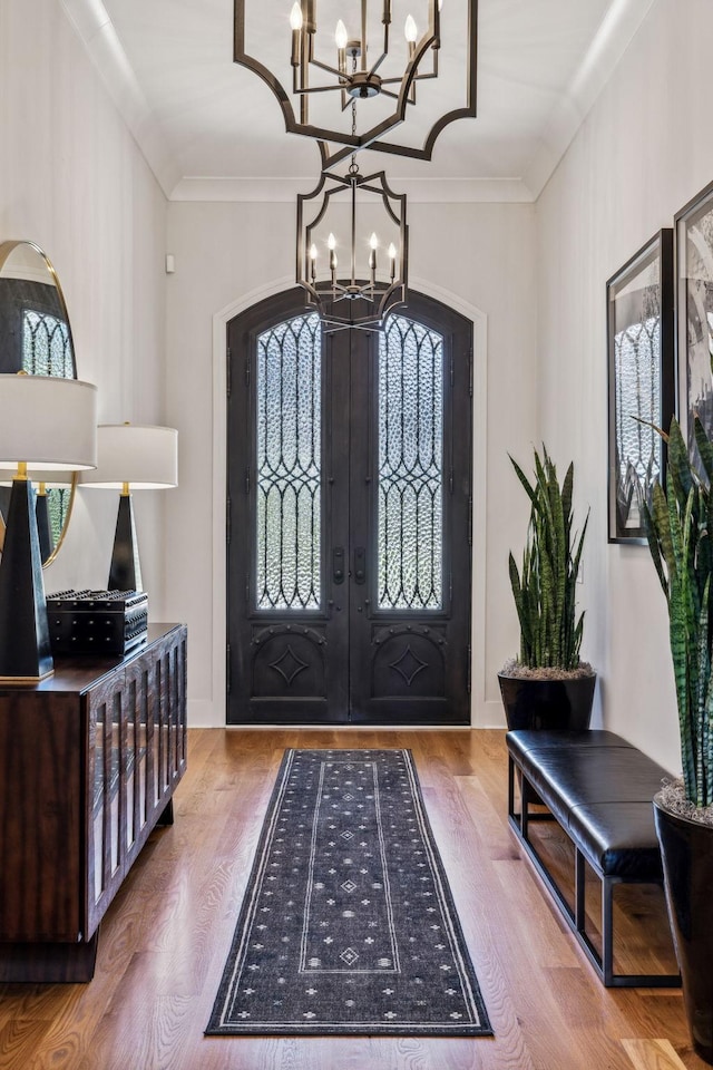 foyer entrance with french doors, a notable chandelier, crown molding, and hardwood / wood-style flooring