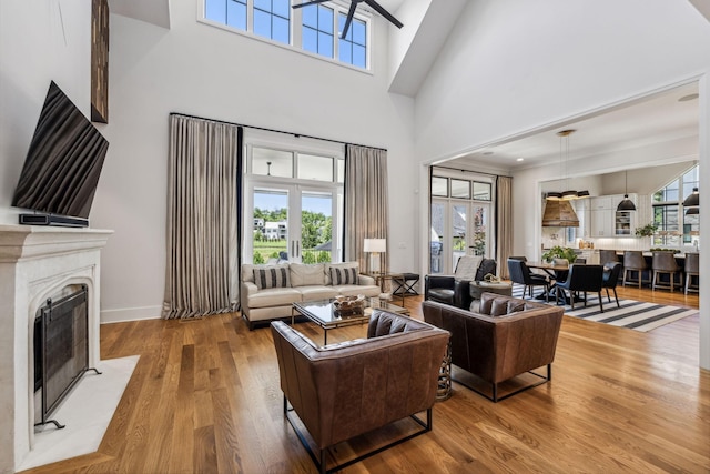 living room featuring ceiling fan, a wealth of natural light, a high ceiling, and light hardwood / wood-style flooring