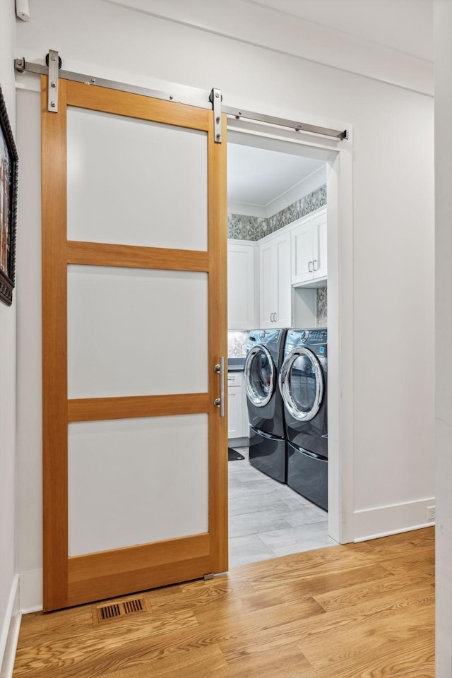 laundry room with washing machine and dryer, cabinets, a barn door, and light hardwood / wood-style flooring