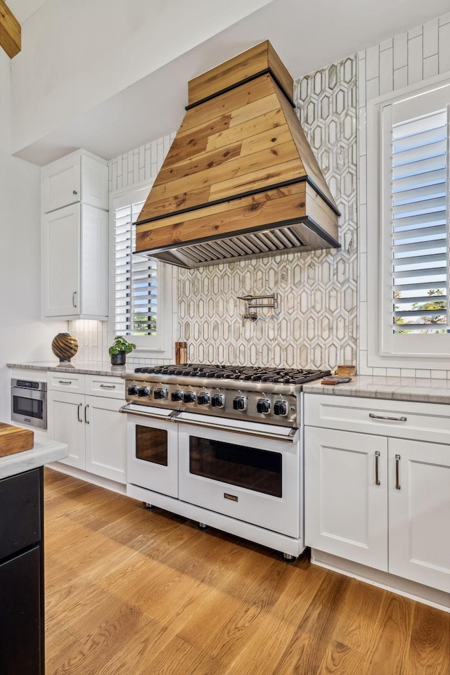 kitchen with backsplash, double oven range, light wood-type flooring, custom range hood, and white cabinets