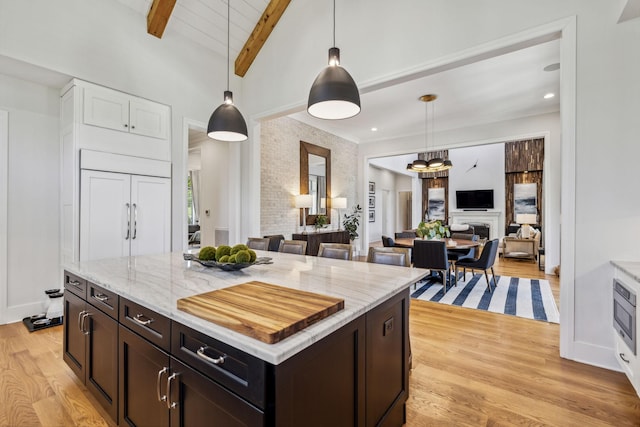 kitchen featuring paneled fridge, a center island, decorative light fixtures, light hardwood / wood-style flooring, and lofted ceiling with beams