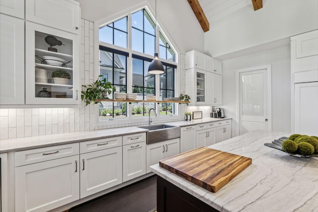 kitchen with vaulted ceiling with beams, white cabinetry, light stone counters, and sink