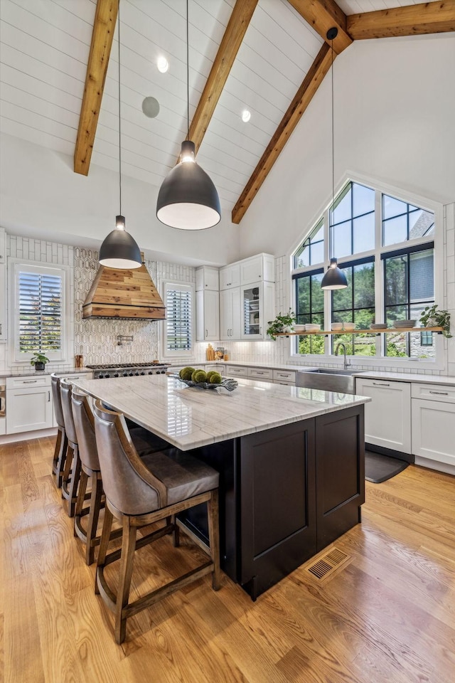 kitchen with decorative backsplash, white cabinetry, a large island, high vaulted ceiling, and custom range hood