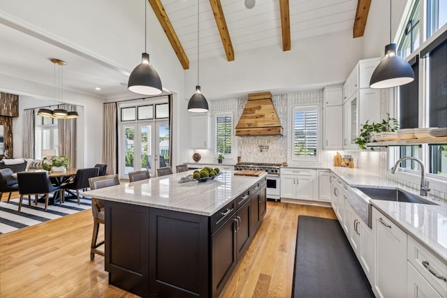 kitchen with decorative light fixtures, backsplash, stainless steel stove, custom exhaust hood, and white cabinets