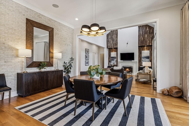 dining area with light wood-type flooring, brick wall, crown molding, and a chandelier