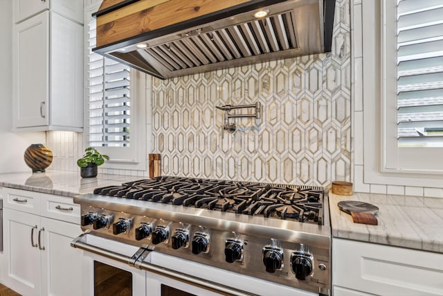 kitchen featuring white cabinets, light stone countertops, range with two ovens, and custom range hood