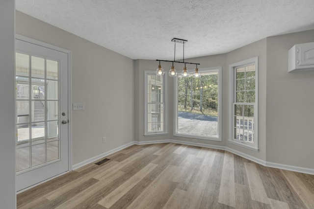 unfurnished dining area with light wood-type flooring and a textured ceiling