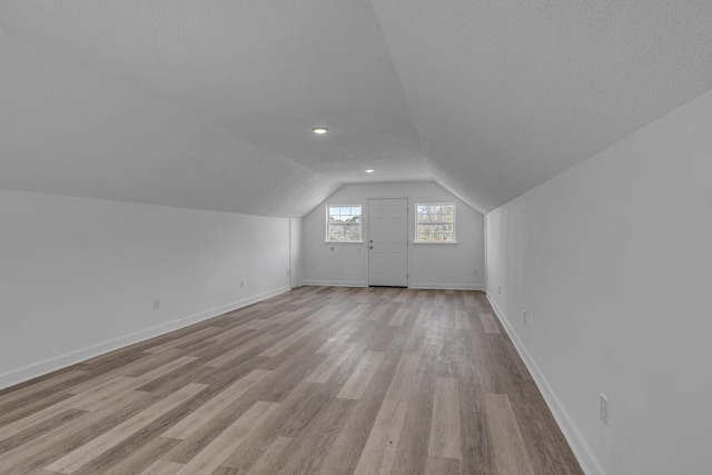 additional living space featuring vaulted ceiling, a textured ceiling, and light hardwood / wood-style flooring