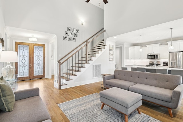 living room with ceiling fan, light hardwood / wood-style floors, ornamental molding, and french doors