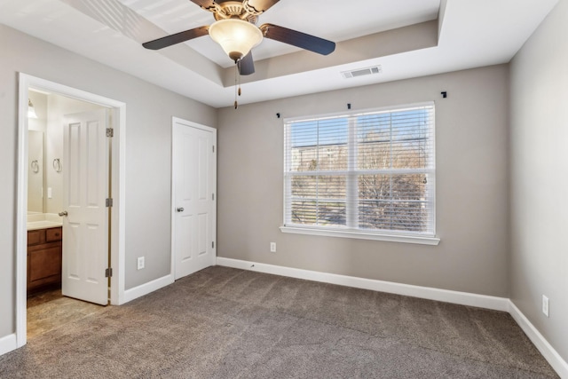 unfurnished bedroom featuring ceiling fan, light colored carpet, a tray ceiling, and connected bathroom