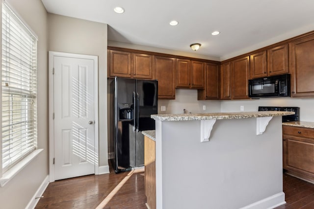 kitchen featuring black appliances, a kitchen breakfast bar, light stone counters, and a kitchen island