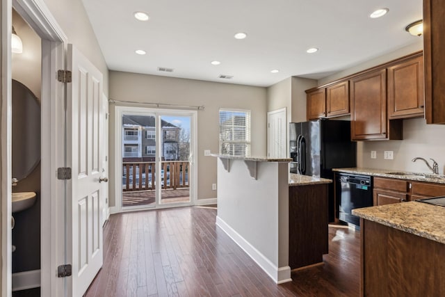 kitchen featuring dark hardwood / wood-style floors, black appliances, sink, light stone countertops, and a breakfast bar area