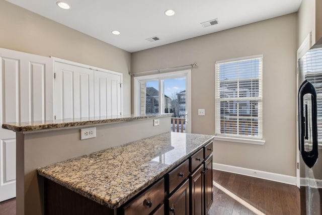 kitchen featuring light stone countertops, dark hardwood / wood-style flooring, dark brown cabinets, and a center island