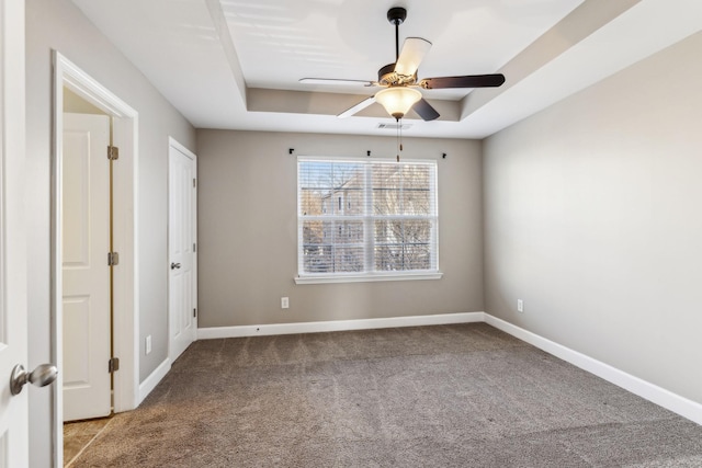 carpeted empty room with a raised ceiling and ceiling fan