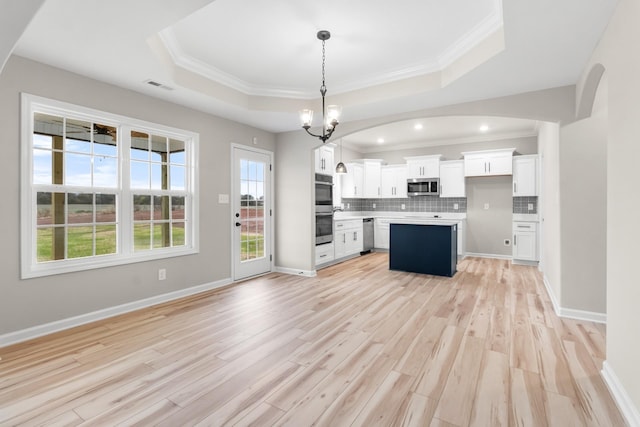 kitchen with appliances with stainless steel finishes, a raised ceiling, white cabinets, and hanging light fixtures