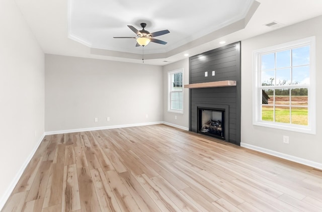 unfurnished living room featuring plenty of natural light, a large fireplace, a tray ceiling, and light wood-type flooring