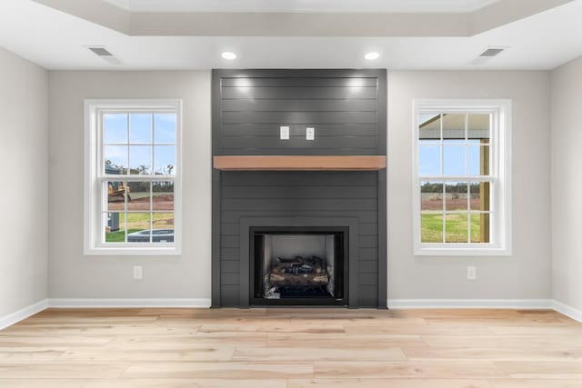 unfurnished living room featuring light hardwood / wood-style floors, a wealth of natural light, and a tray ceiling