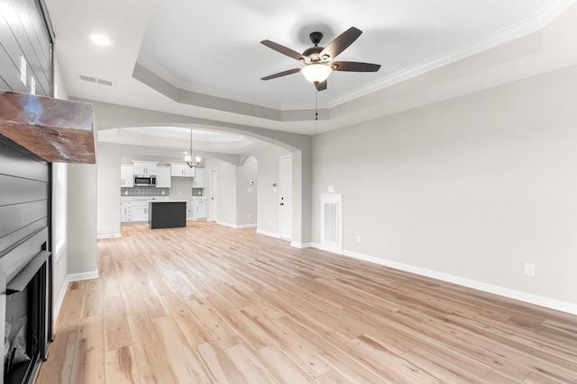 unfurnished living room with ceiling fan with notable chandelier, light hardwood / wood-style floors, crown molding, and a raised ceiling