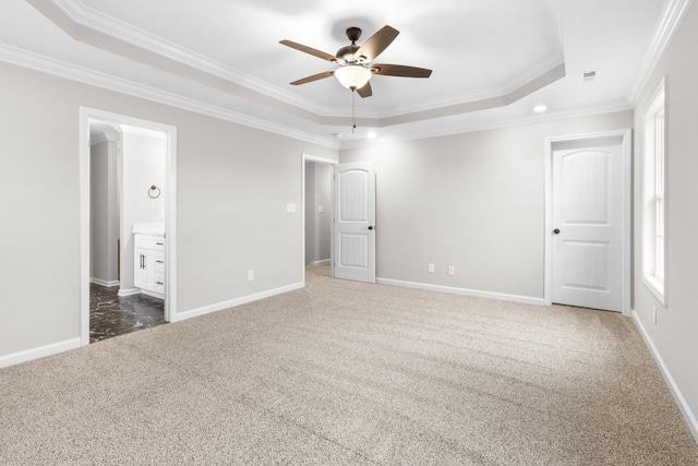 unfurnished bedroom with ceiling fan, ensuite bathroom, crown molding, a tray ceiling, and dark colored carpet