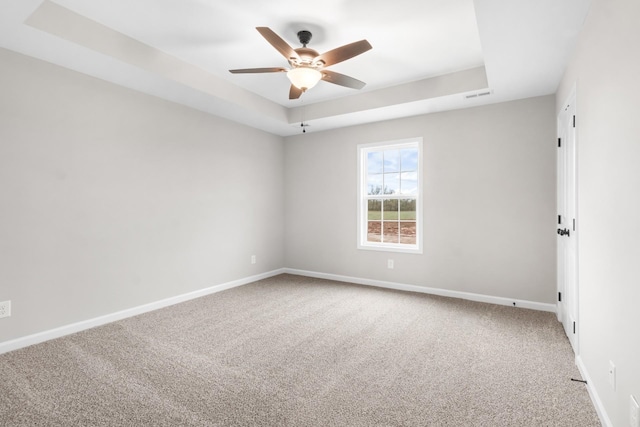 carpeted spare room featuring a raised ceiling and ceiling fan