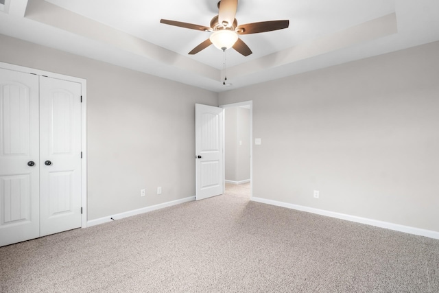 unfurnished bedroom with ceiling fan, a closet, carpet floors, and a tray ceiling