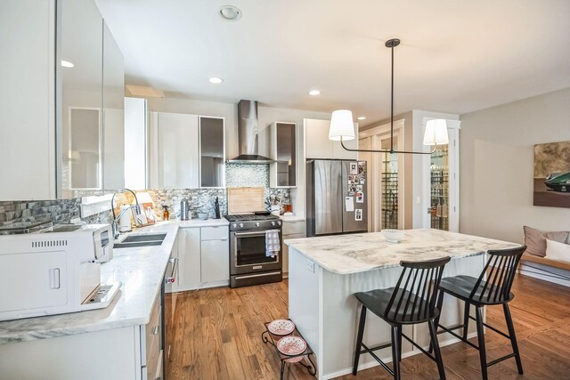 kitchen featuring appliances with stainless steel finishes, a center island, wall chimney range hood, tasteful backsplash, and hanging light fixtures