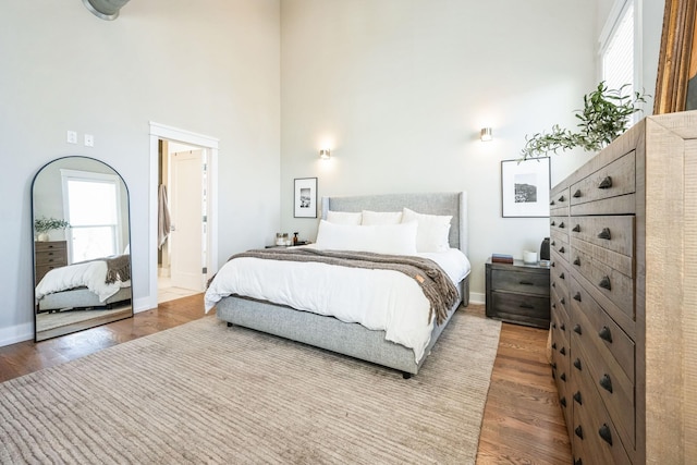 bedroom featuring hardwood / wood-style flooring, multiple windows, and a towering ceiling