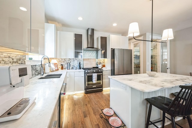 kitchen with white cabinets, wall chimney exhaust hood, stainless steel appliances, and pendant lighting