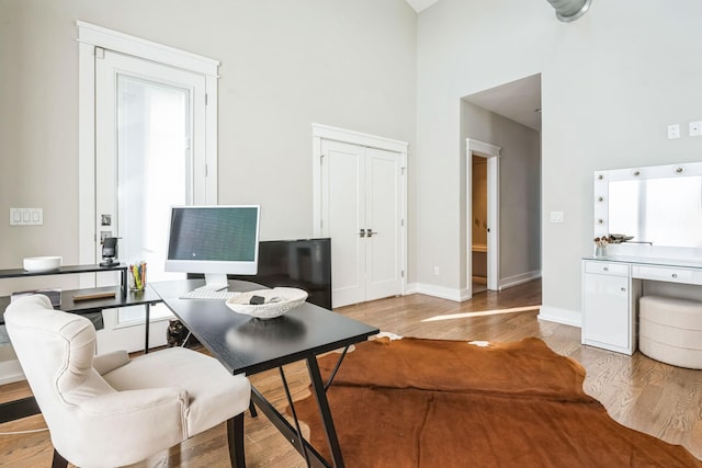 home office featuring light wood-type flooring and a high ceiling