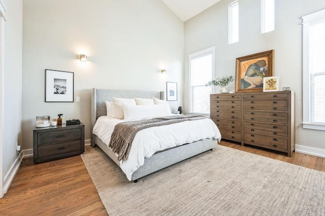 bedroom featuring high vaulted ceiling, multiple windows, and hardwood / wood-style flooring