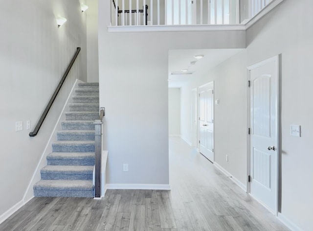 stairway with wood-type flooring and a towering ceiling