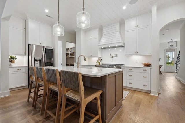 kitchen with a kitchen island with sink, sink, premium range hood, and white cabinetry