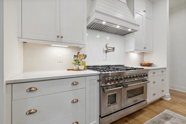 kitchen with light hardwood / wood-style flooring, premium range hood, white cabinetry, and range with two ovens