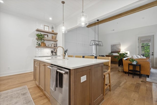 kitchen with decorative light fixtures, sink, light wood-type flooring, stainless steel dishwasher, and a center island with sink