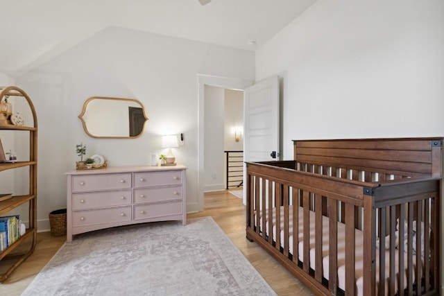 bedroom featuring light wood-type flooring, lofted ceiling, and a crib