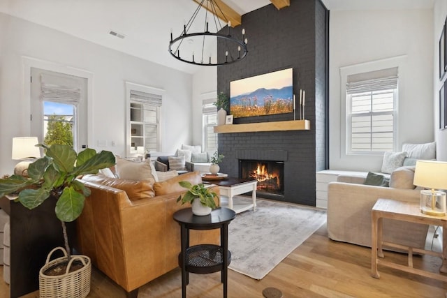 living room featuring a healthy amount of sunlight, a brick fireplace, a notable chandelier, and hardwood / wood-style floors