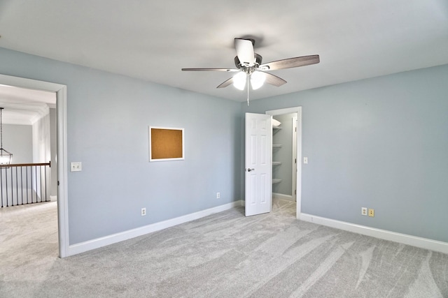 unfurnished bedroom featuring a spacious closet, a closet, light carpet, and ceiling fan