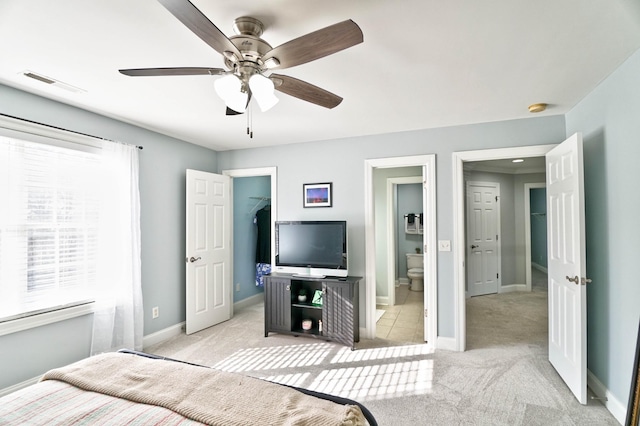 carpeted bedroom with ceiling fan, ensuite bathroom, a walk in closet, and multiple windows