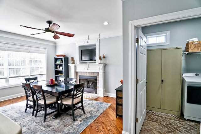 dining area with a brick fireplace, ornamental molding, washer / clothes dryer, and ceiling fan