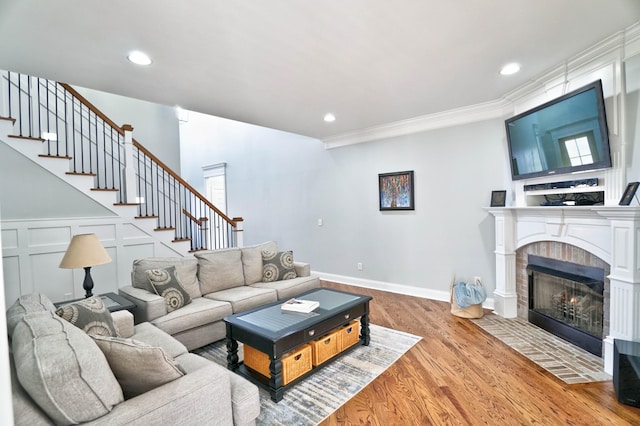 living room featuring a tiled fireplace, crown molding, and hardwood / wood-style floors