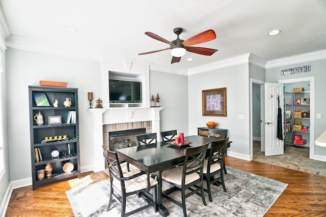 dining area with ceiling fan, wood-type flooring, a brick fireplace, and ornamental molding