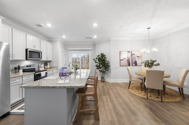 kitchen featuring white cabinets, decorative light fixtures, stainless steel appliances, a kitchen island with sink, and light stone counters