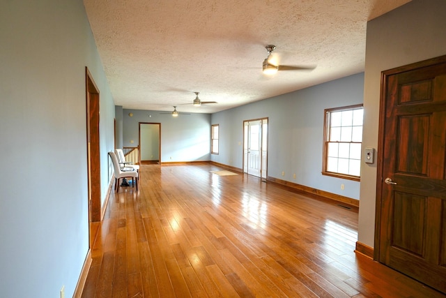 empty room with a textured ceiling, ceiling fan, and light hardwood / wood-style flooring