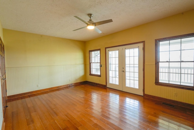 empty room featuring ceiling fan, a textured ceiling, hardwood / wood-style flooring, and french doors